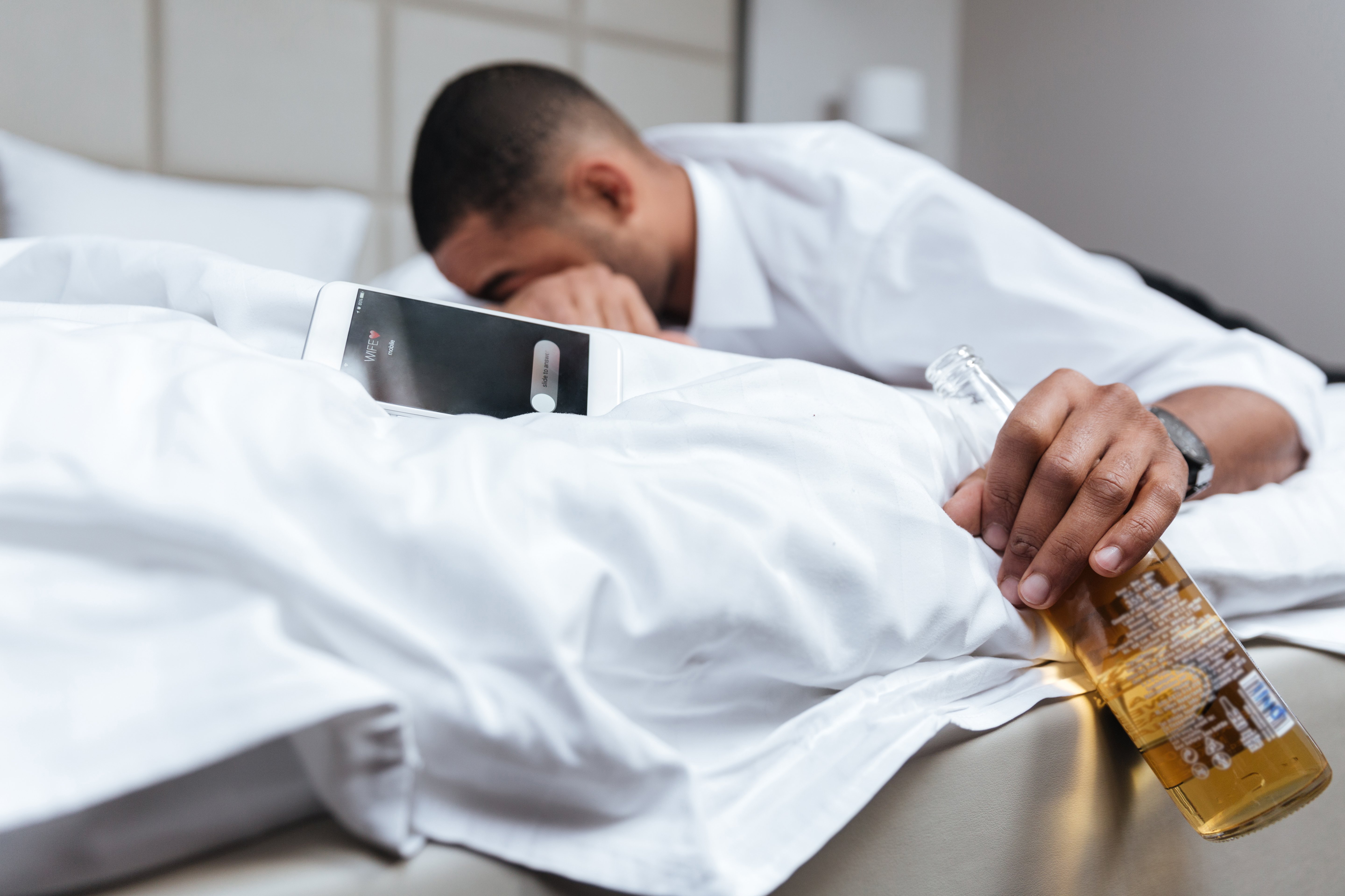 graphicstock-drunk-young-african-man-in-shirt-sleeping-on-bed-and-holding-bottle-of-beer-in-hand-focus-on-bottle-side-view_SdZp24pL2x